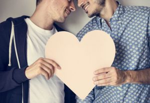 Two men looking at each other and holding a cut out heart shape