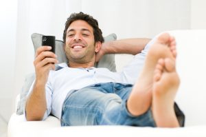 Young smiling man laying on the sofa messaging on his mobile phone at home.