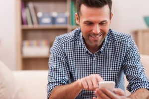 Man in check shirt smiling whilst looking at mobile phone